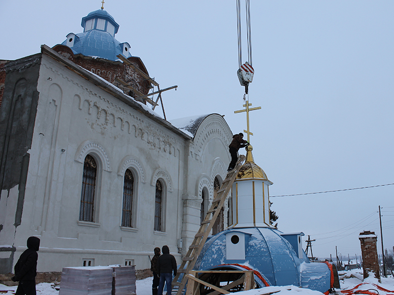 Рабочий крепит новый сверкающий двухметровый крест на купол храмовой колокольни