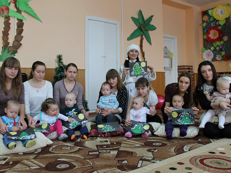 Молодые мамы со своими малышами из открывшейся в этом году студии раннего развития детей украшают нарисованные ёлочки