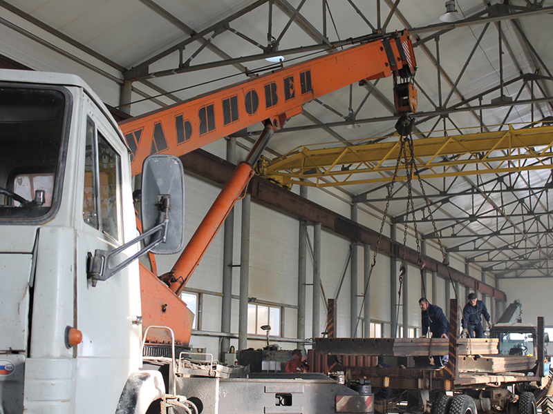 Рабочие цеха транспортируют с помощью автокрана тяжёлые металлические платформы